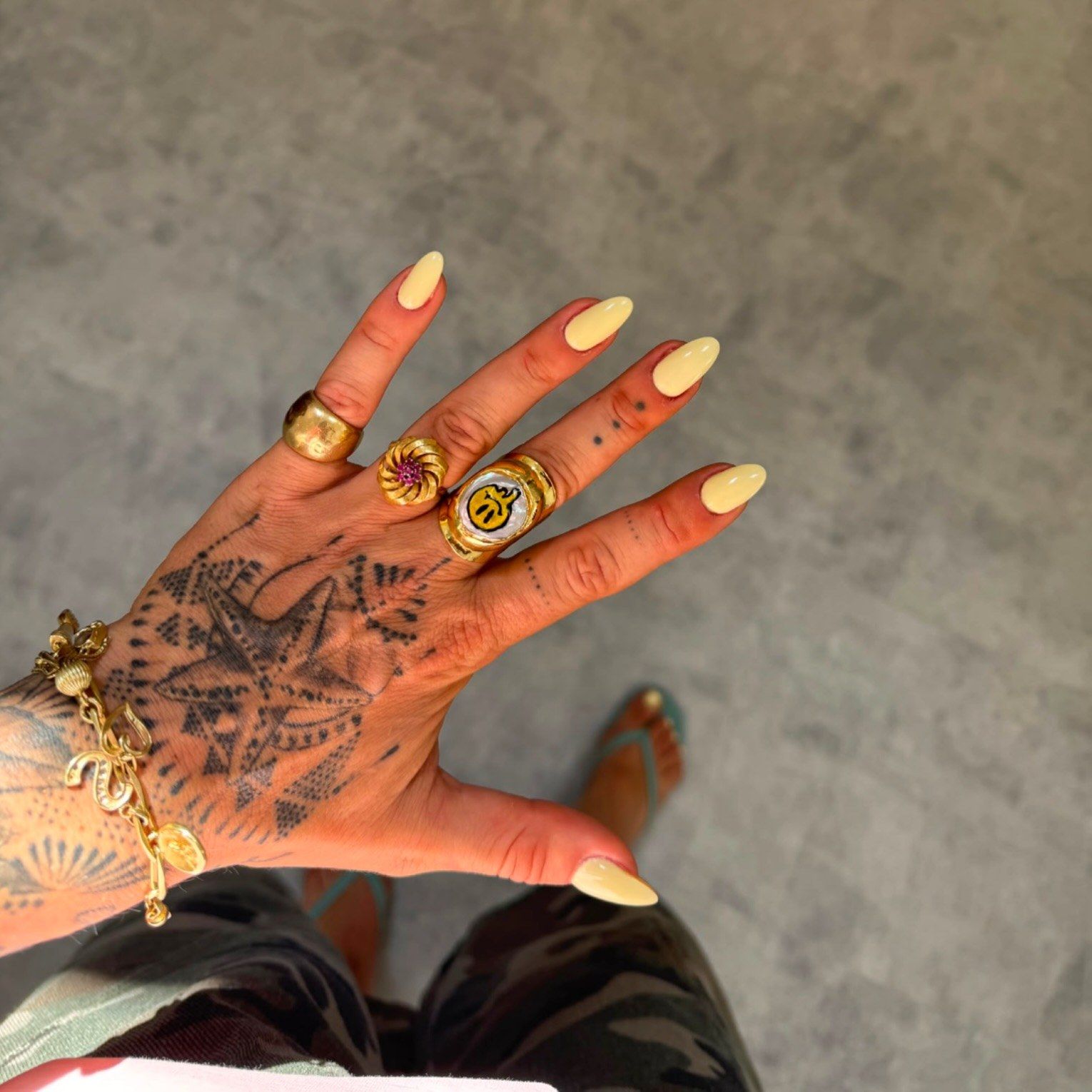 Pastelgele nagels op een hand met tatoeages en gouden ringen