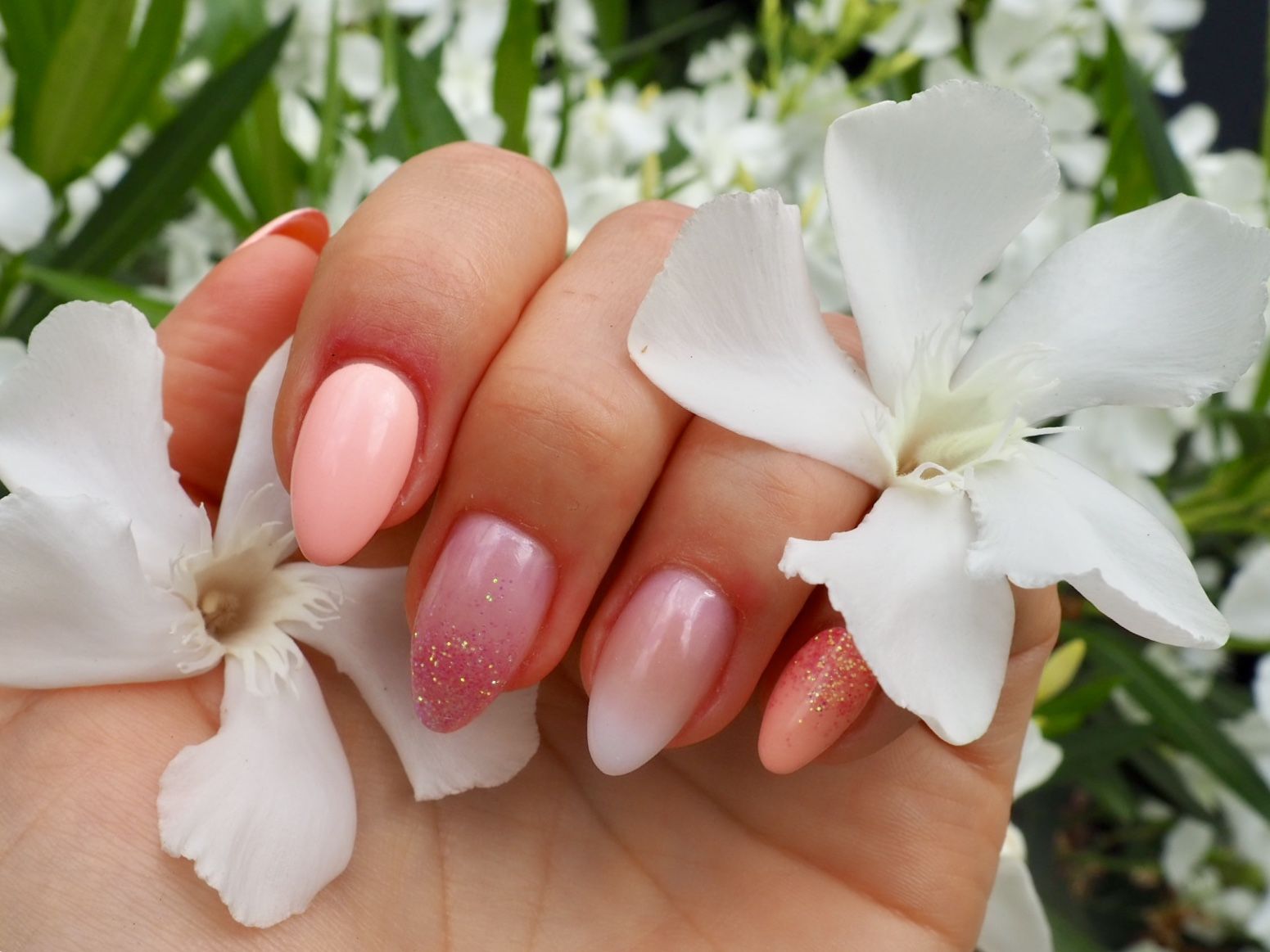 Zachtroze amandelnagels met glitter ombre en witte bloemen